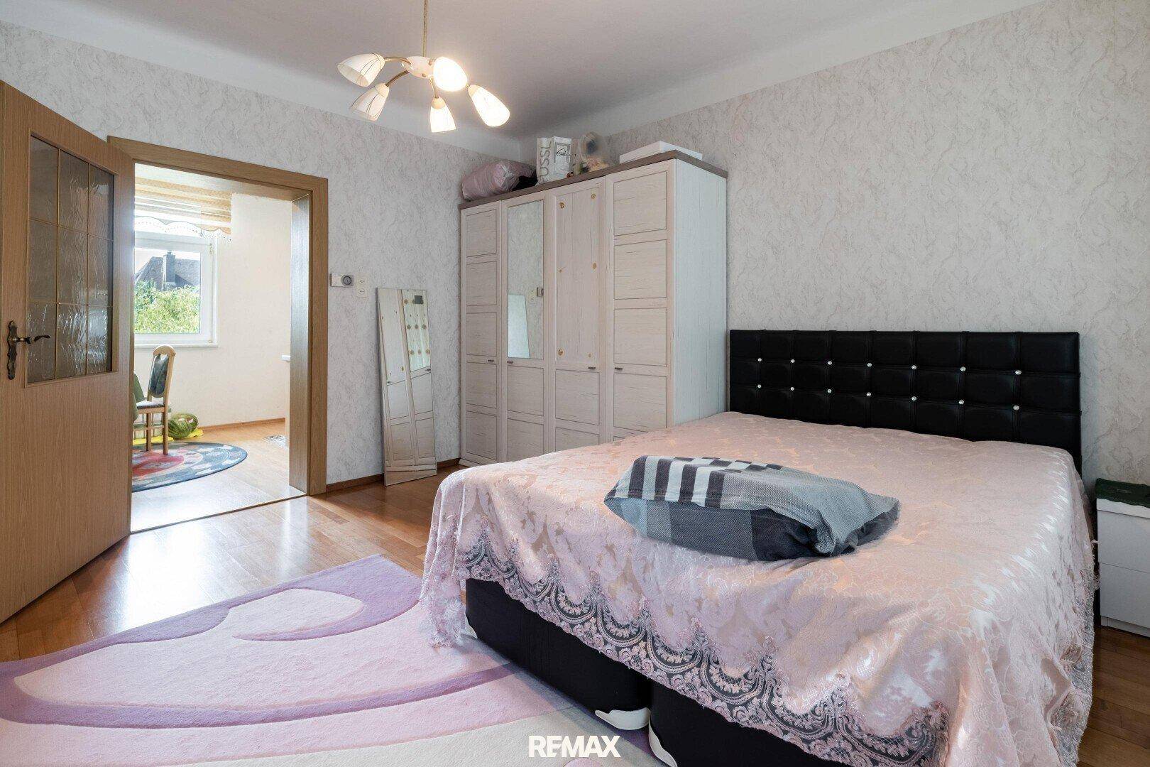 Schlafzimmer mit Doppelbett, großem Kleiderschrank und Parkettboden, verbunden mit einem weiteren Raum.