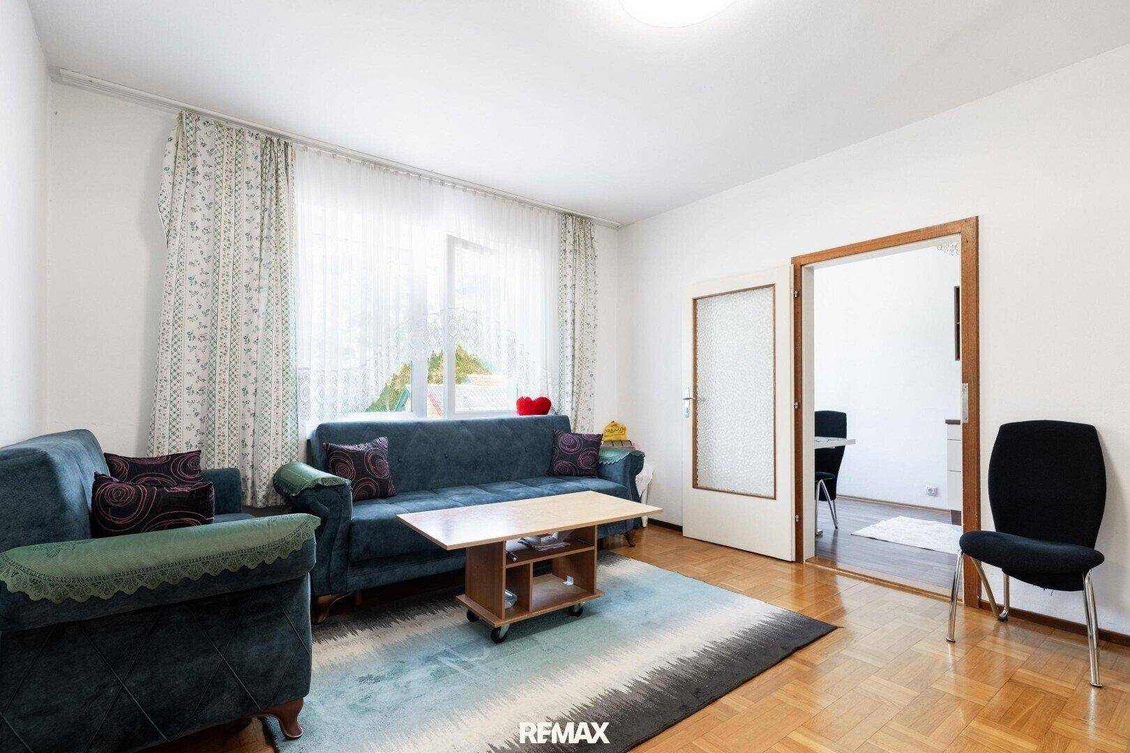 Helles Wohnzimmer mit blauen Sofas, Holzboden und einem Teppich in modernen Farben.