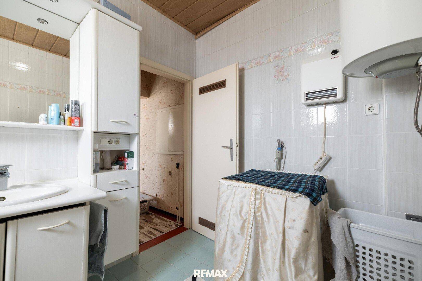 Badezimmer mit Waschbecken, Schränken und Platz für eine Waschmaschine, gefliest in hellen Farben.