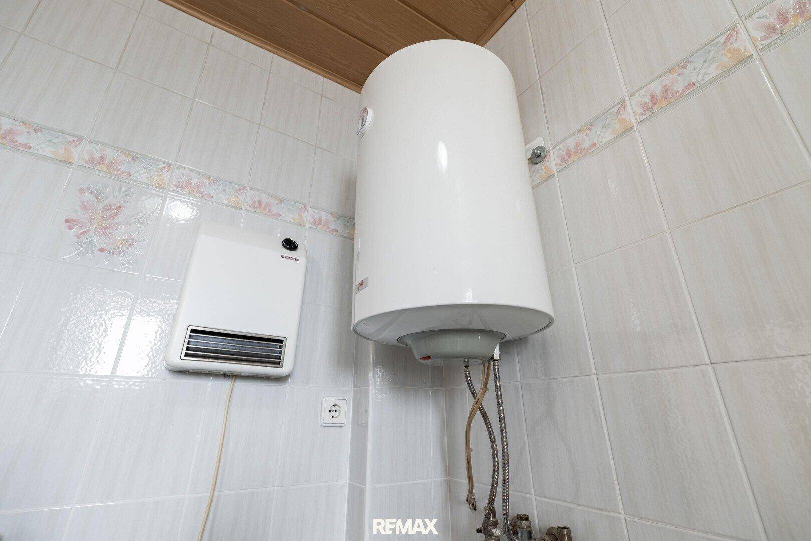 Wandmontierter Warmwasserbereiter und Heizlüfter in einem gefliesten Raum.