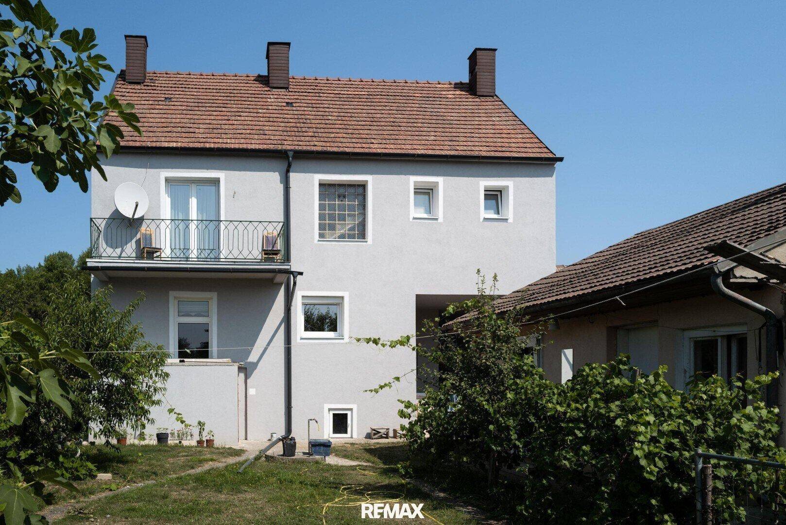 Rückansicht des Wohnhauses mit Balkon und Gartenbereich unter blauem Himmel.