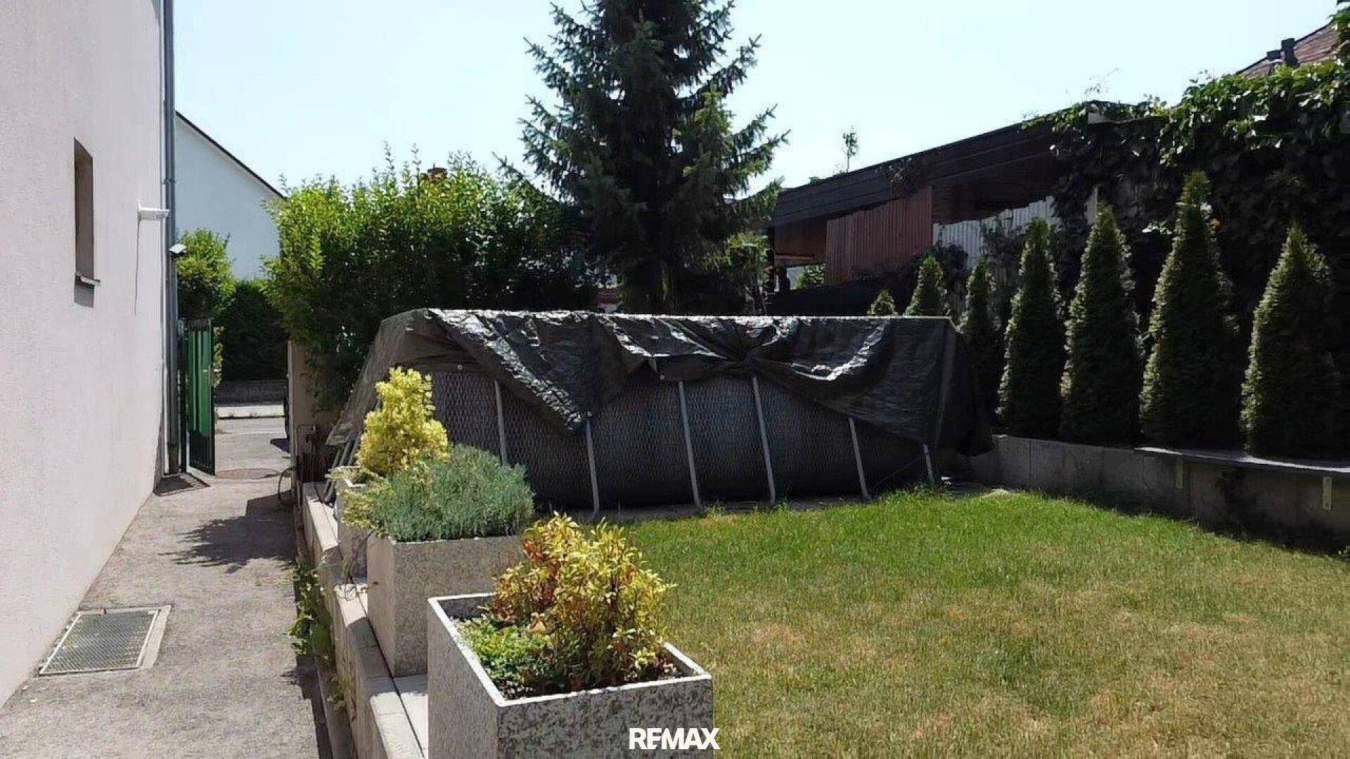Gartenbereich mit Rasenfläche und einem abgedeckten Aufstellpool im Freien.