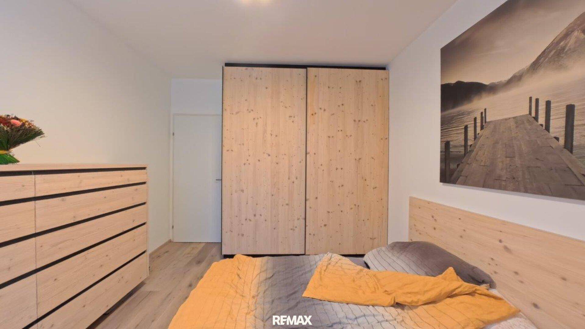Schlafzimmer mit Holzbett, integriertem Kleiderschrank und hellem Laminatboden.