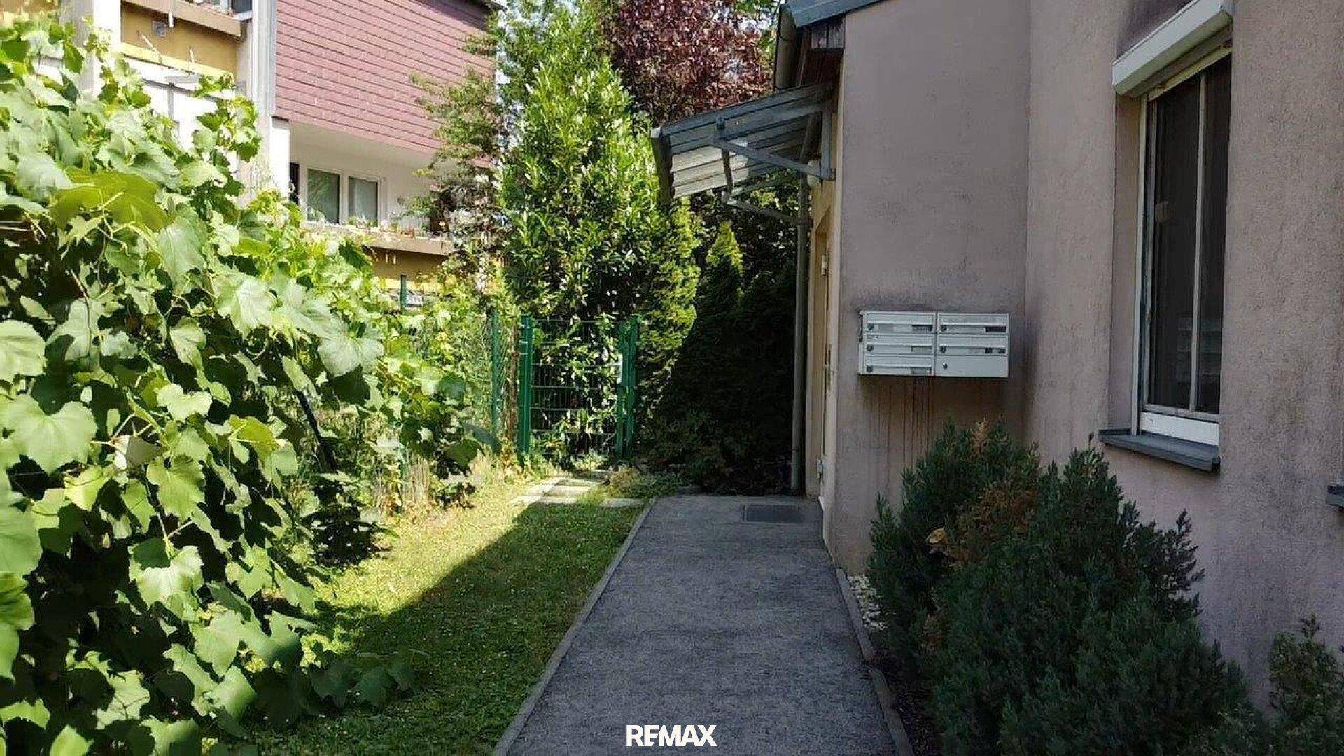 Eingangsbereich des Hauses mit einem gepflasterten Weg und üppiger Vegetation im Vorgarten.