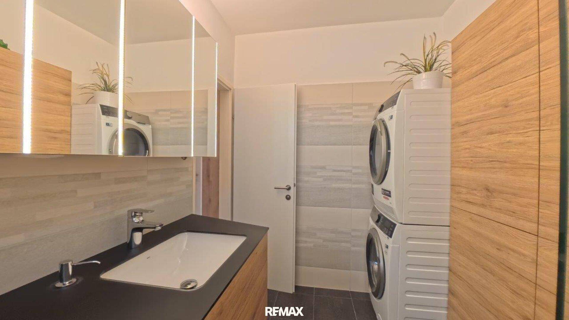 Badezimmer mit Waschmaschine und Trockner, Einzelwaschbecken und Spiegelschrank.