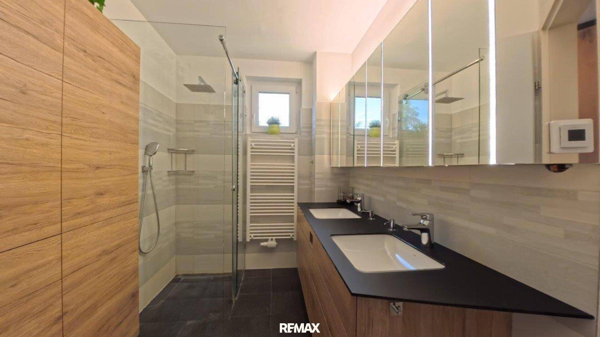 Modernes Badezimmer mit Doppelwaschbecken, großer Dusche und Holzschränken.