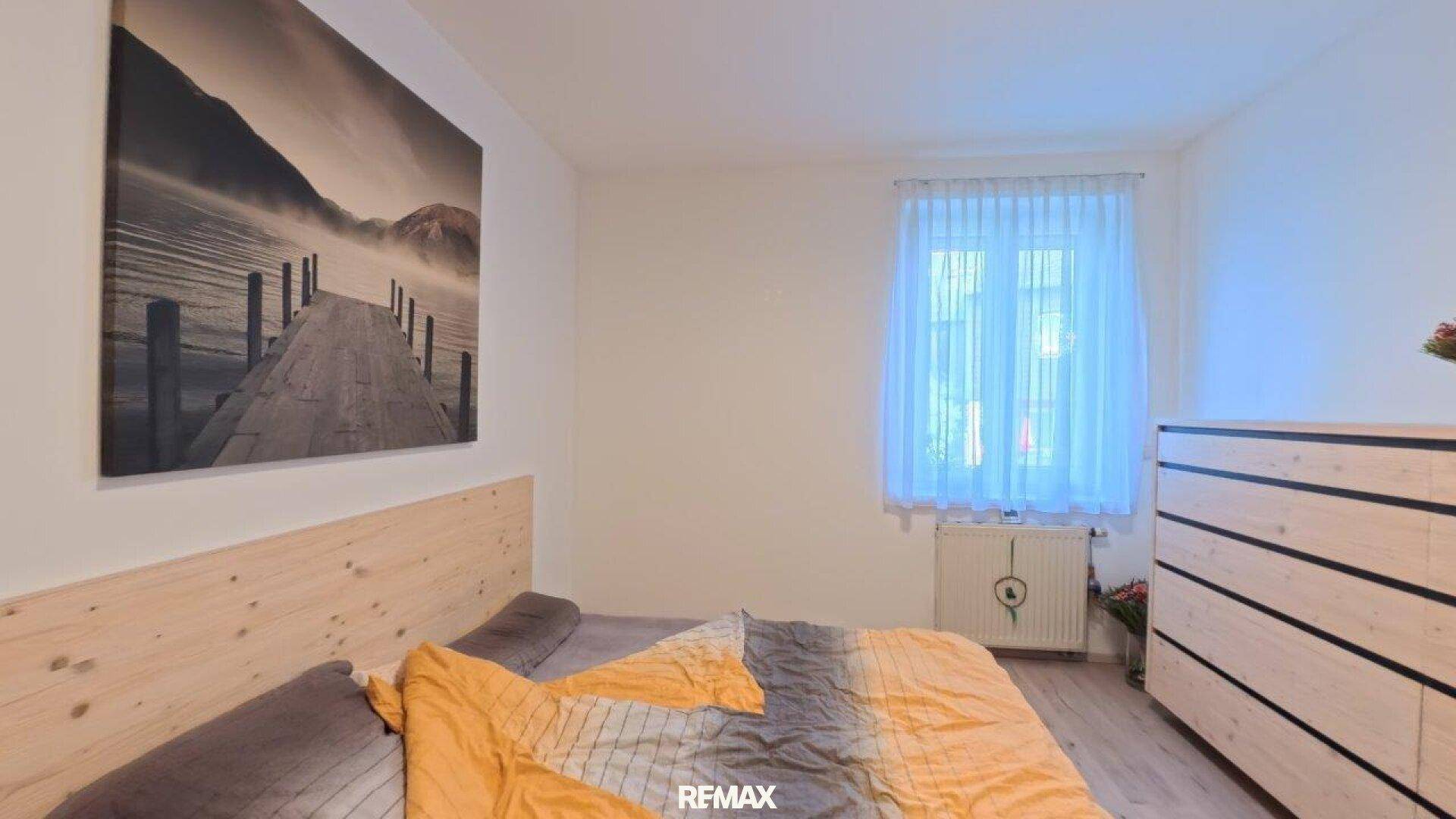 Gemütliches Schlafzimmer mit Holzbett, Kommode und großem Wandbild über dem Bett.