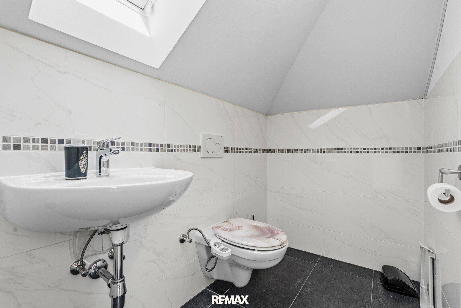Kleines WC im Dachgeschoss mit Waschbecken, Wand-WC und Dachfenster.