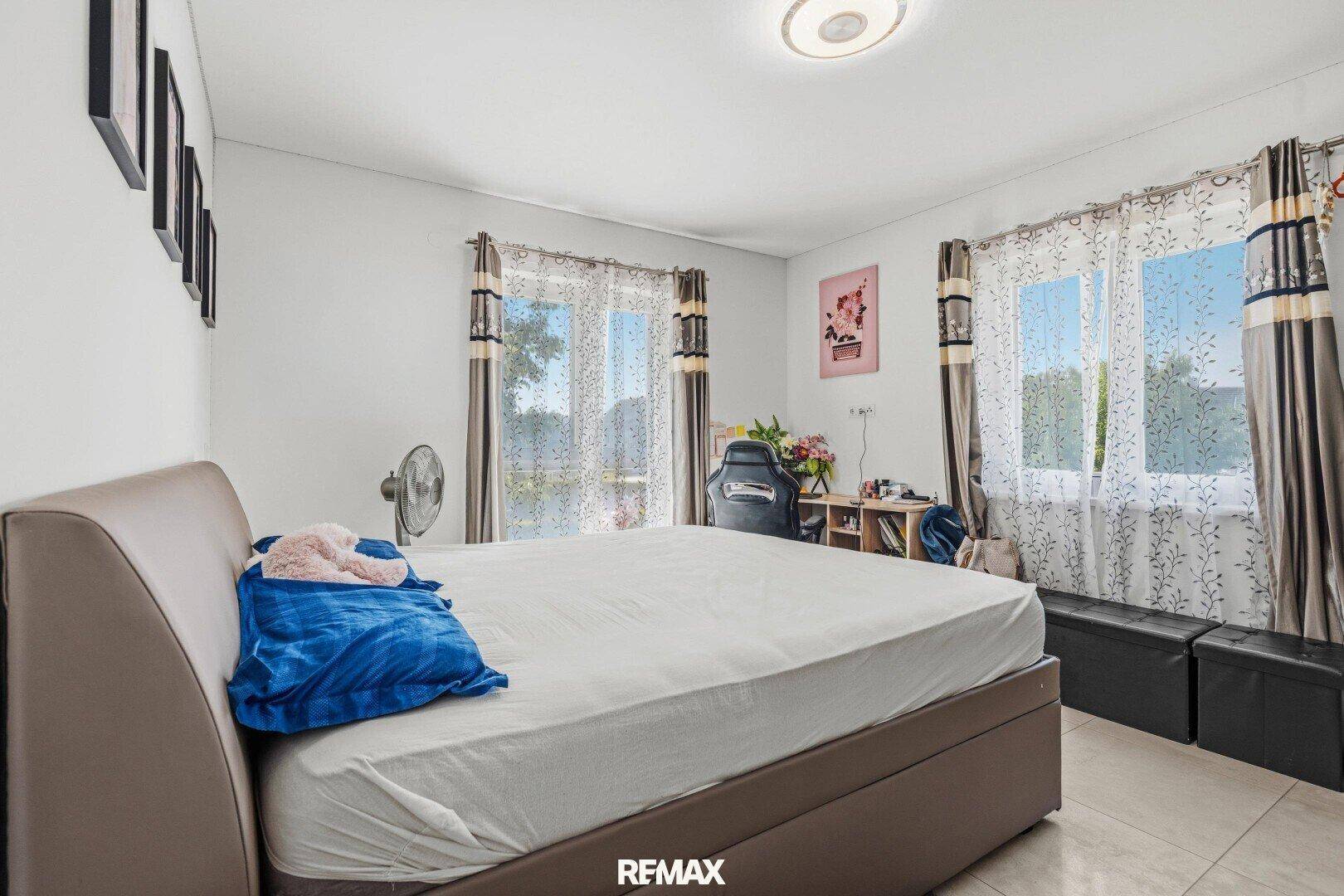 Geräumiges Schlafzimmer mit Doppelbett, Fliesenboden und zwei großen Fenstern.
