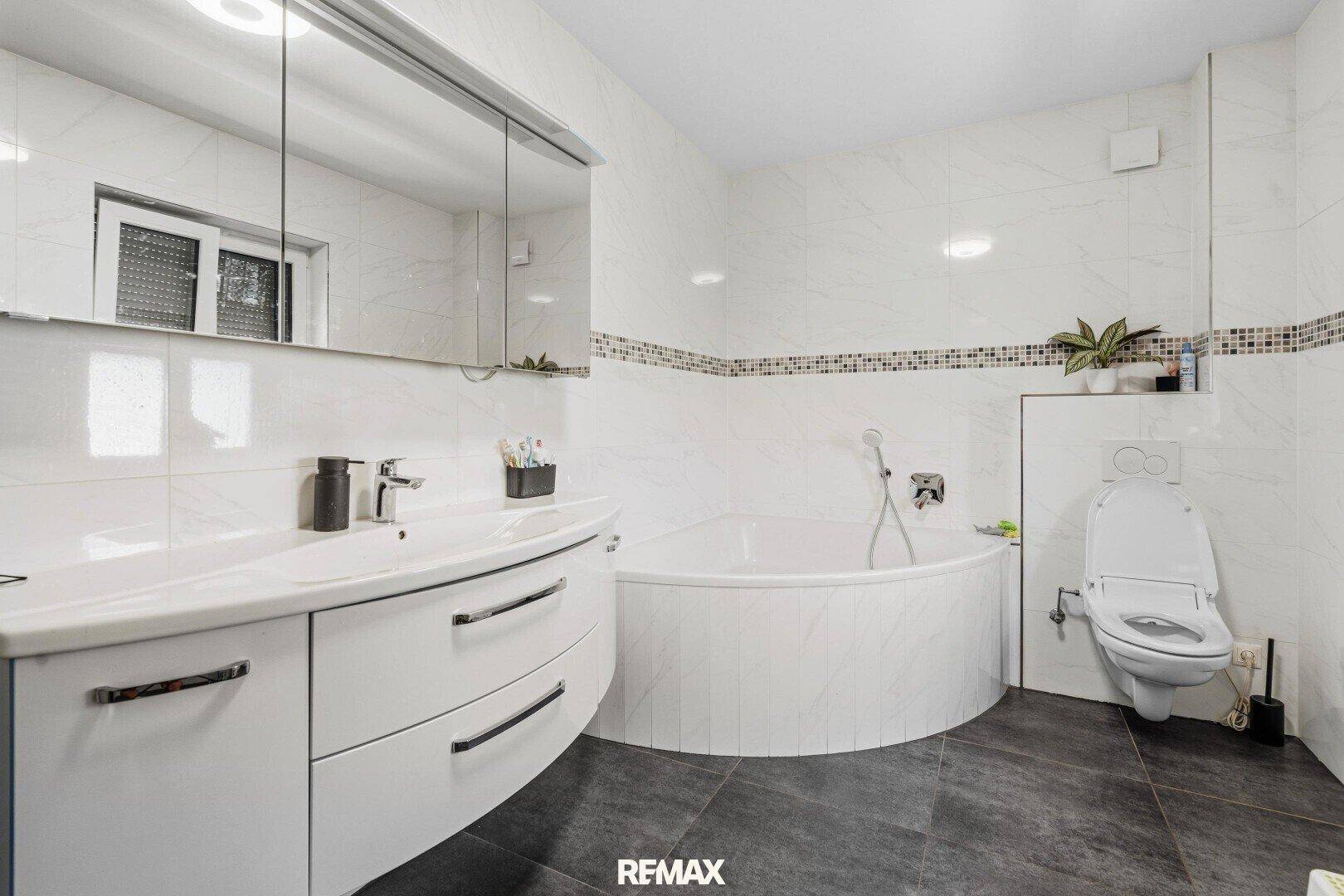 Modernes Badezimmer mit Badewanne, Wand-WC, Einzelwaschbecken und Spiegelschrank.