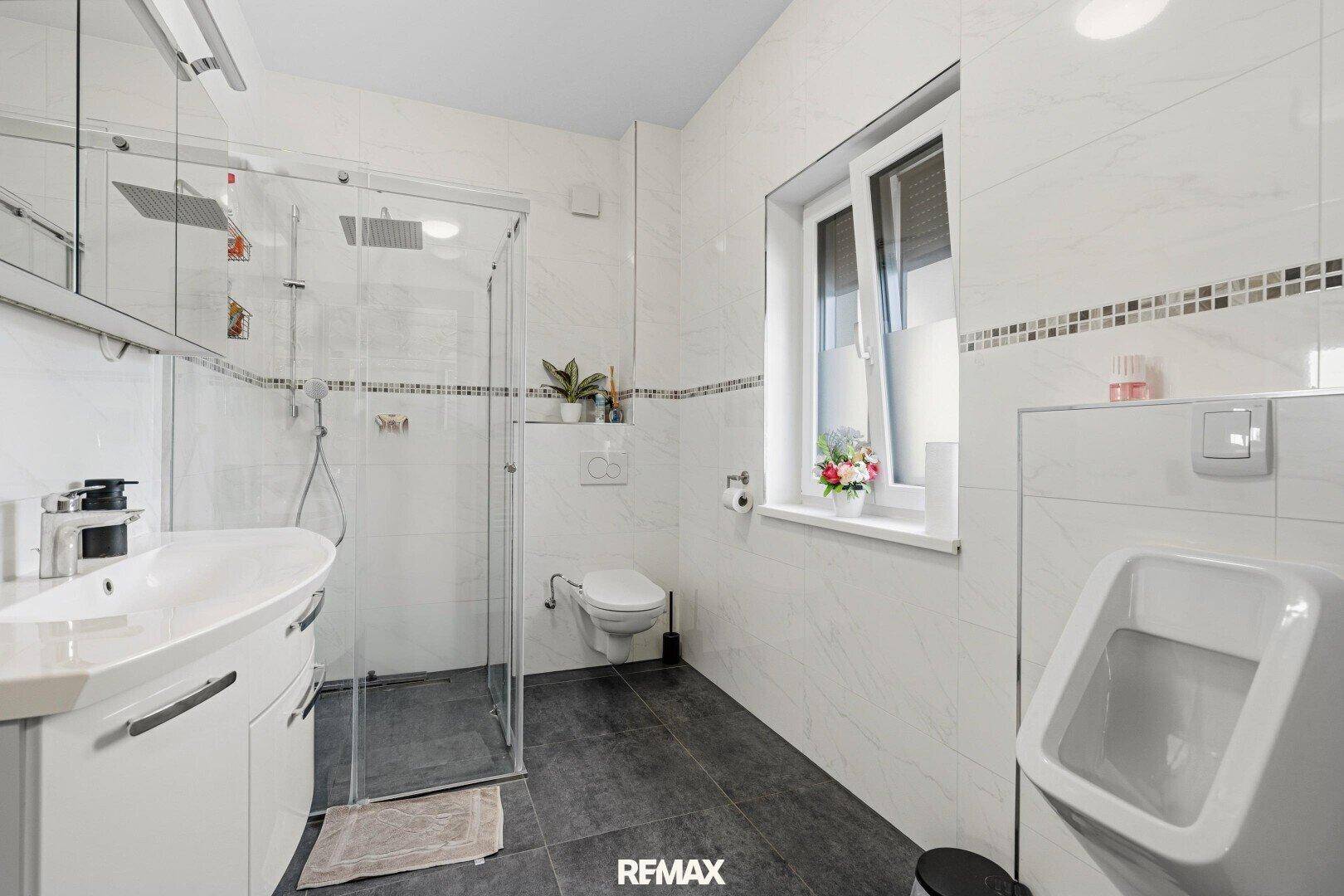 Modernes Badezimmer mit Duschkabine, Urinal, Wand-WC und Fenster.
