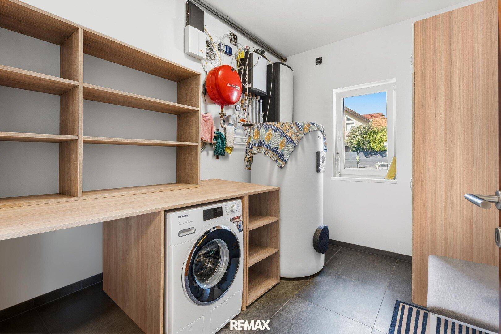 Praktischer Hauswirtschaftsraum mit Waschmaschine, Regalen und Warmwasserboiler.