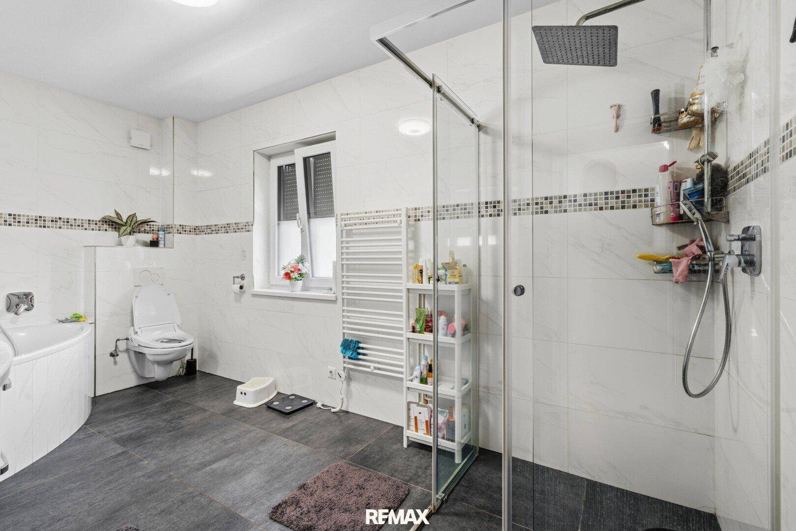 Geräumiges Badezimmer mit Duschkabine, Badewanne, Wand-WC und beheiztem Handtuchhalter.