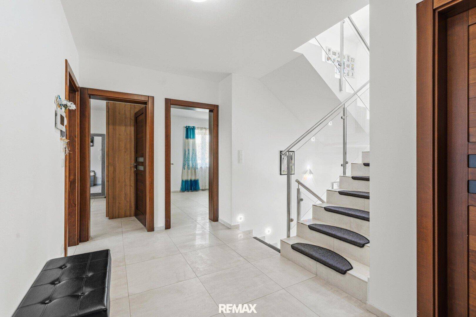 Heller Flur mit moderner Treppe, Glasgeländer und Fliesenboden.