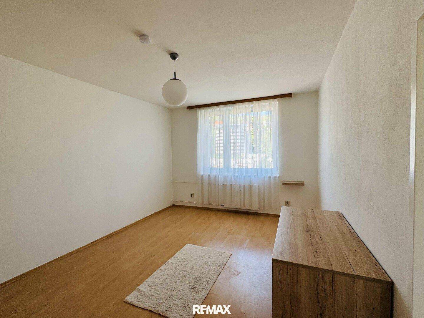 Leeres Schlafzimmer mit Holzboden, weißen Wänden und einem Fenster, das viel Tageslicht hereinlässt.