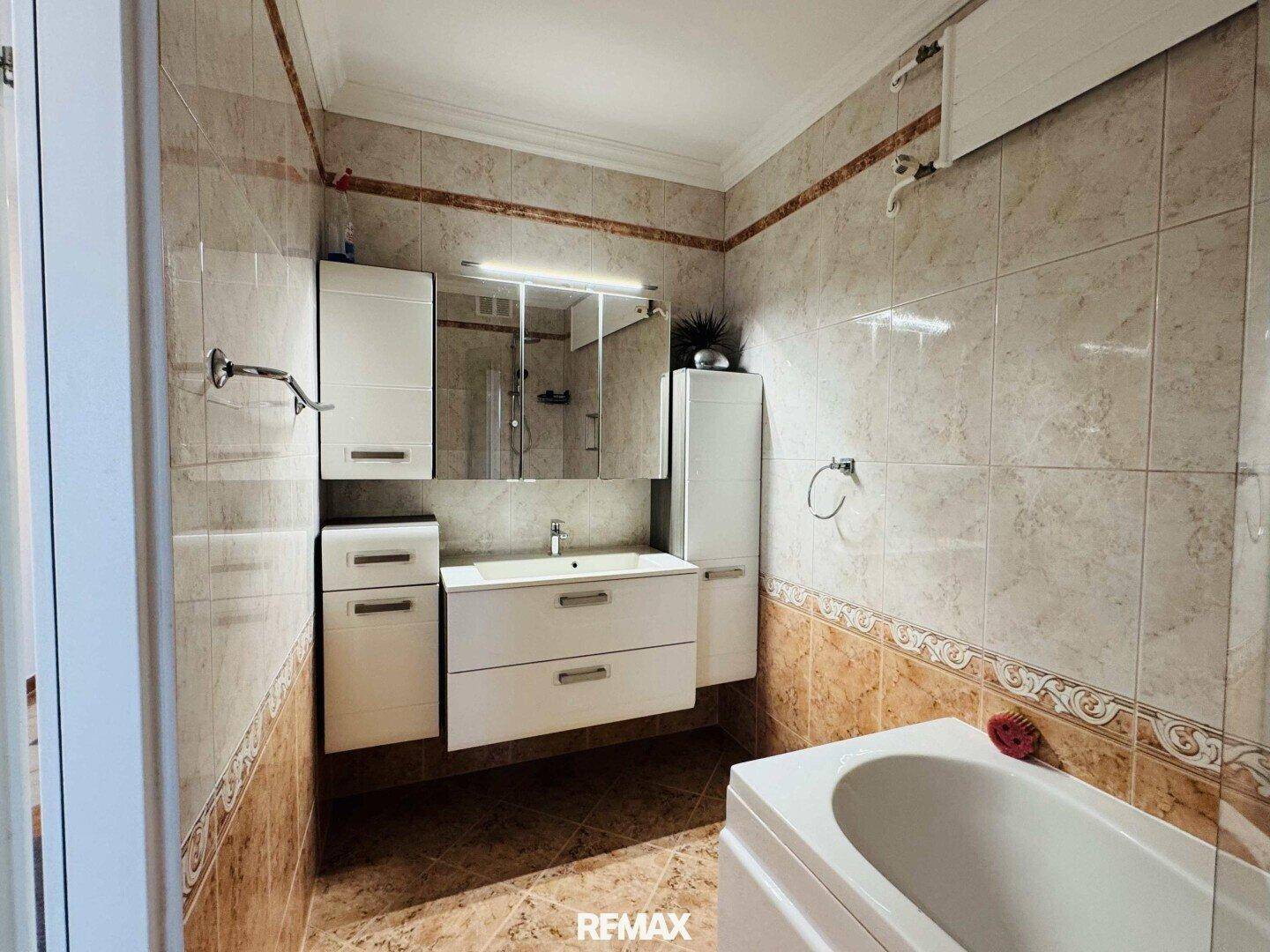Gefliestes Badezimmer mit Badewanne, modernem Waschbeckenunterschrank und Spiegelschrank.