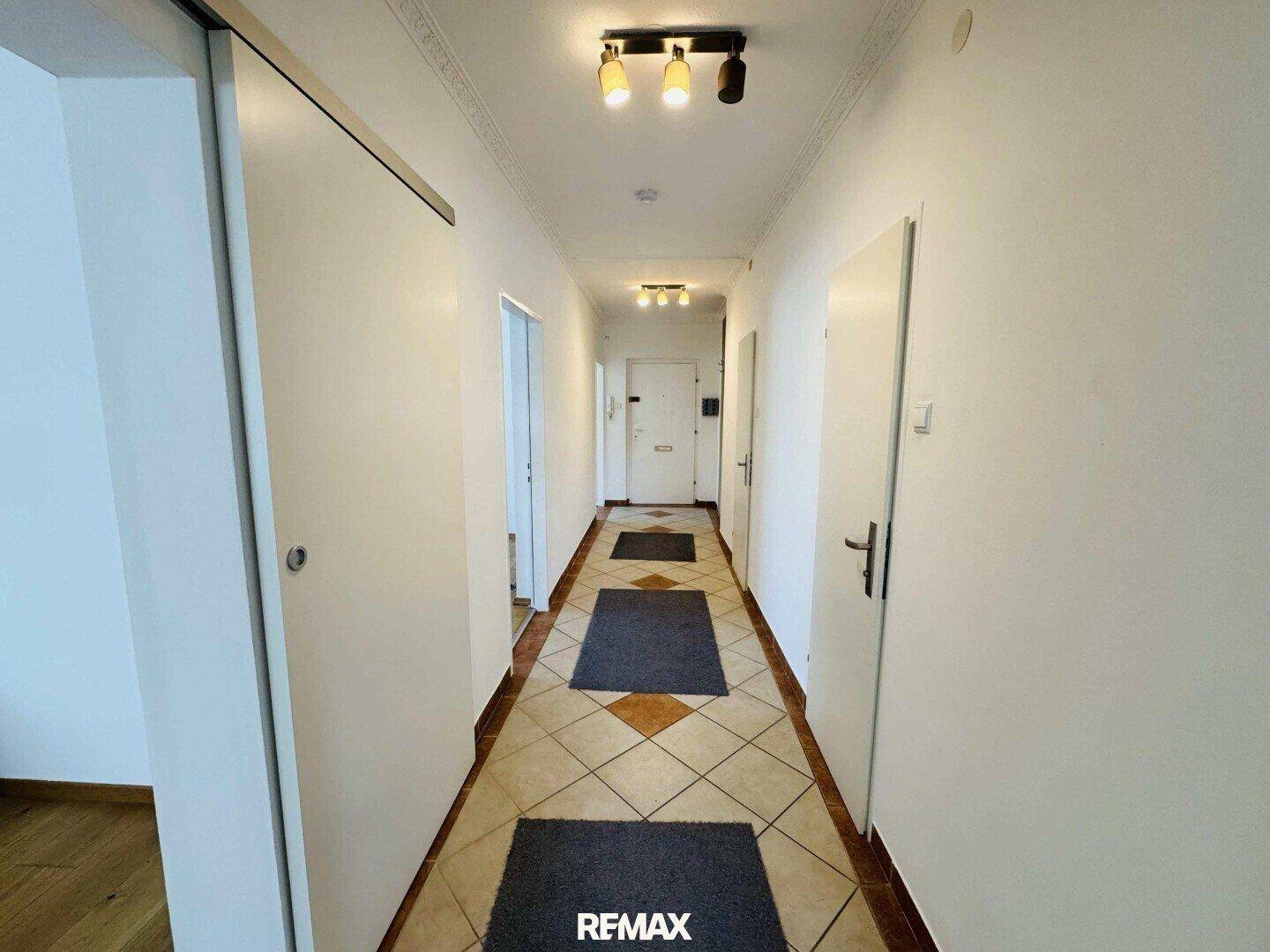 Langer Flur mit Fliesenboden, mehreren Türen und praktischer Deckenbeleuchtung.