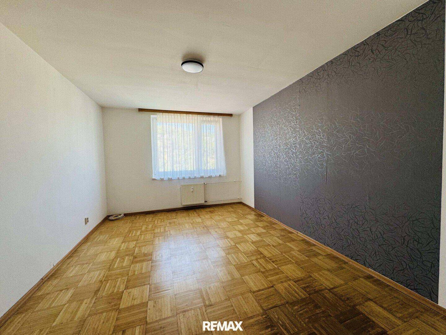 Leeres Zimmer mit Parkettboden und einer dunkelgrauen Akzentwand mit dezentem Muster.