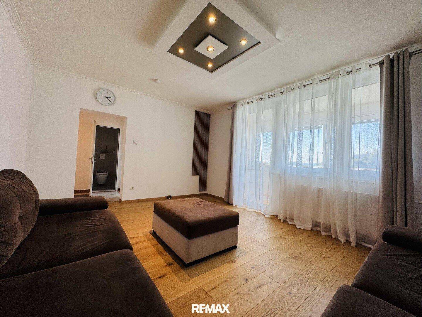 Helles Wohnzimmer mit Holzboden, bequemen Sofas und einer modernen Deckenbeleuchtung.
