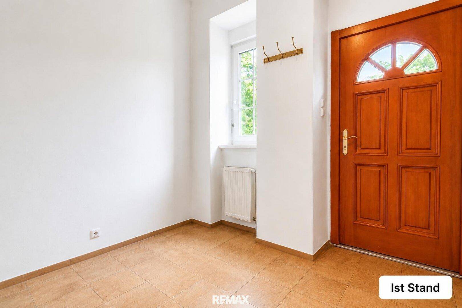 Aktueller Zustand des leeren Eingangsbereichs mit Fliesenboden und einer Holzeingangstür.