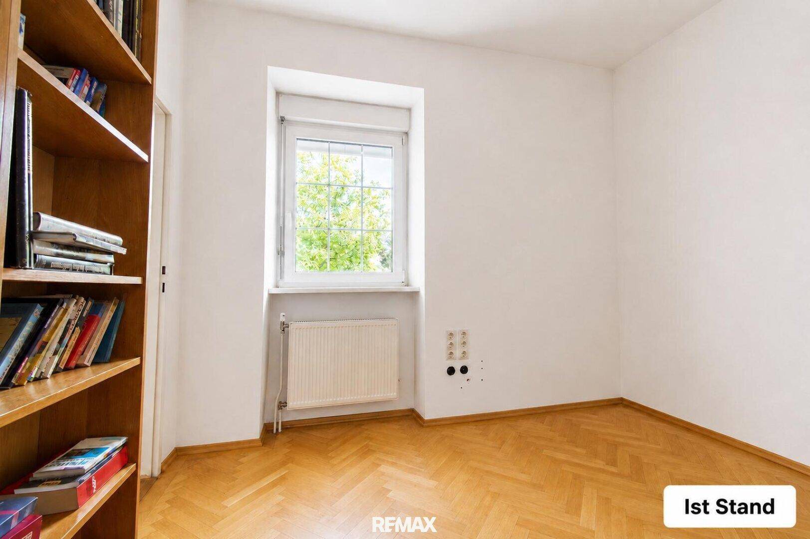 Aktueller Zustand des leeren Raumes mit Bücherregal und Fischgrätparkettboden.