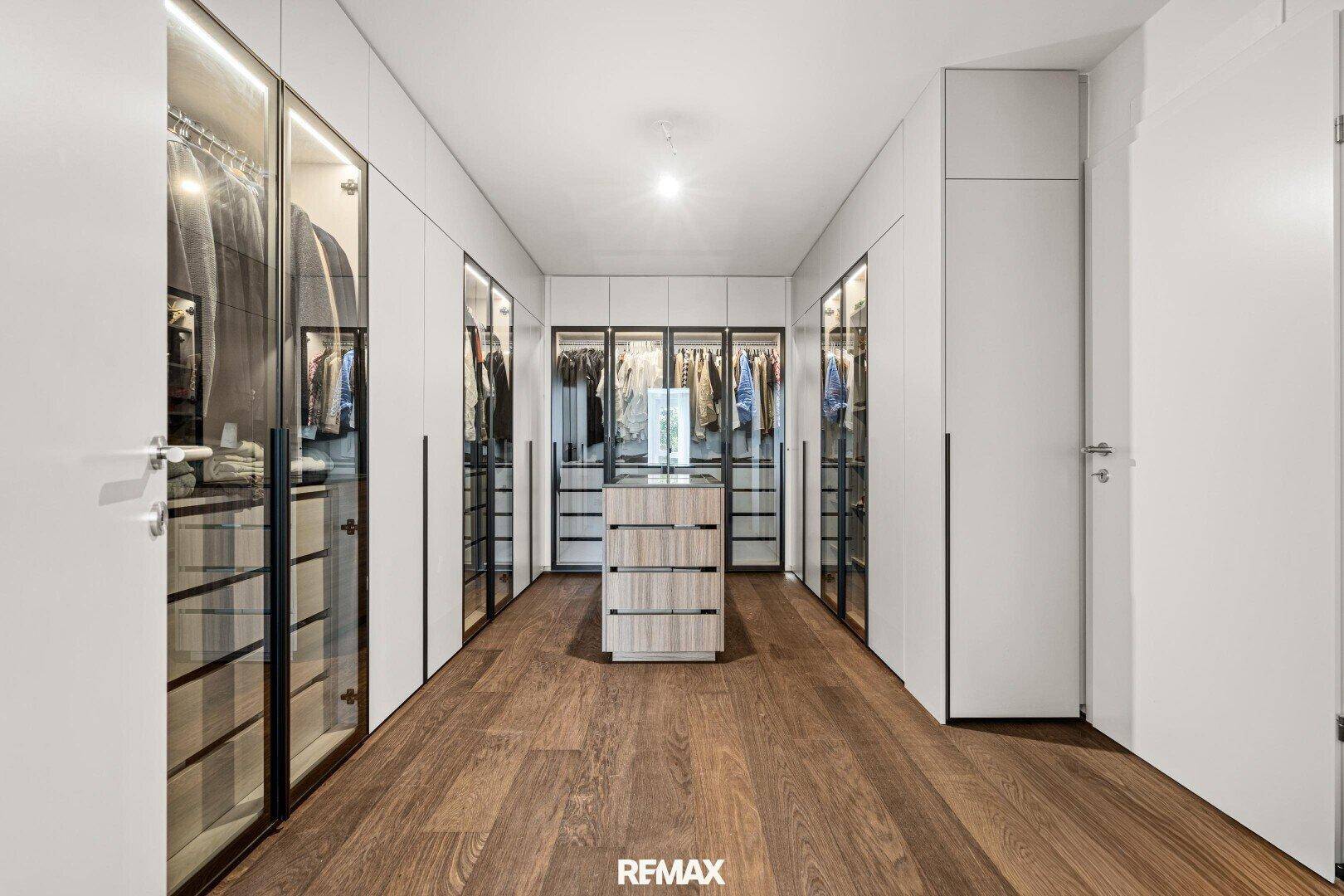Großer begehbarer Kleiderschrank mit Glasfronten und Holzboden.