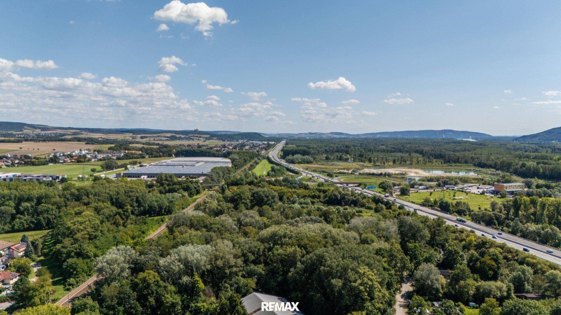 Weitläufige Luftaufnahme der Landschaft mit Autobahn, Wäldern und ländlicher Umgebung unter blauem Himmel.