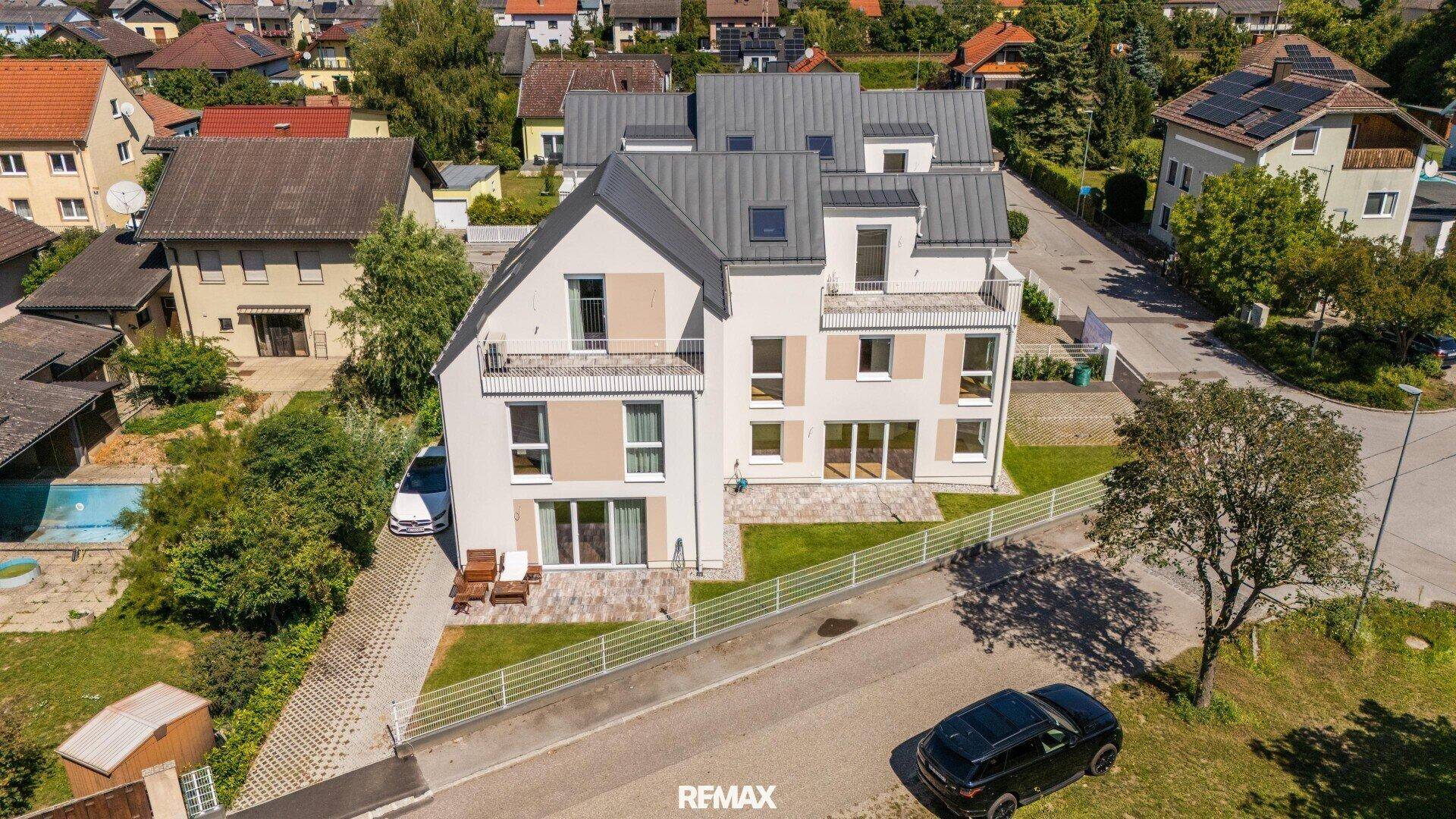 Luftaufnahme eines modernen Neubaus mit Garten und umliegender Wohnbebauung.