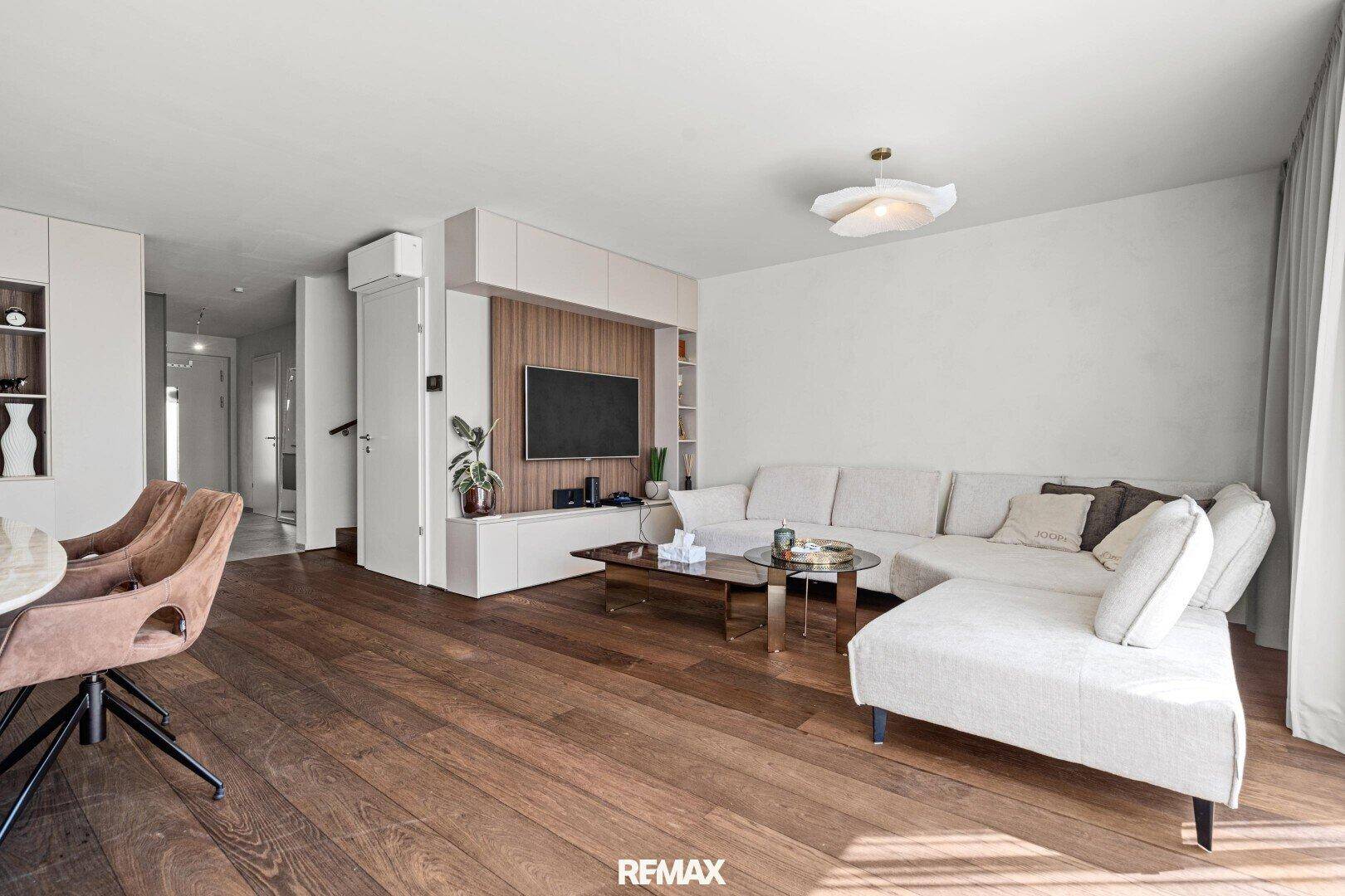 Heller Wohnbereich mit beigem Ecksofa, Holzboden und integriertem TV-Möbel.