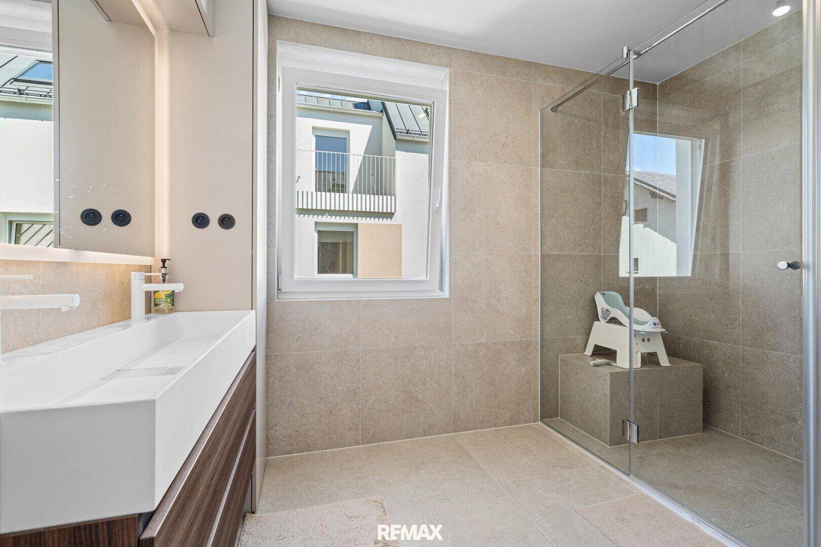 Modernes Badezimmer mit großer Dusche, Waschtisch und Fenster.