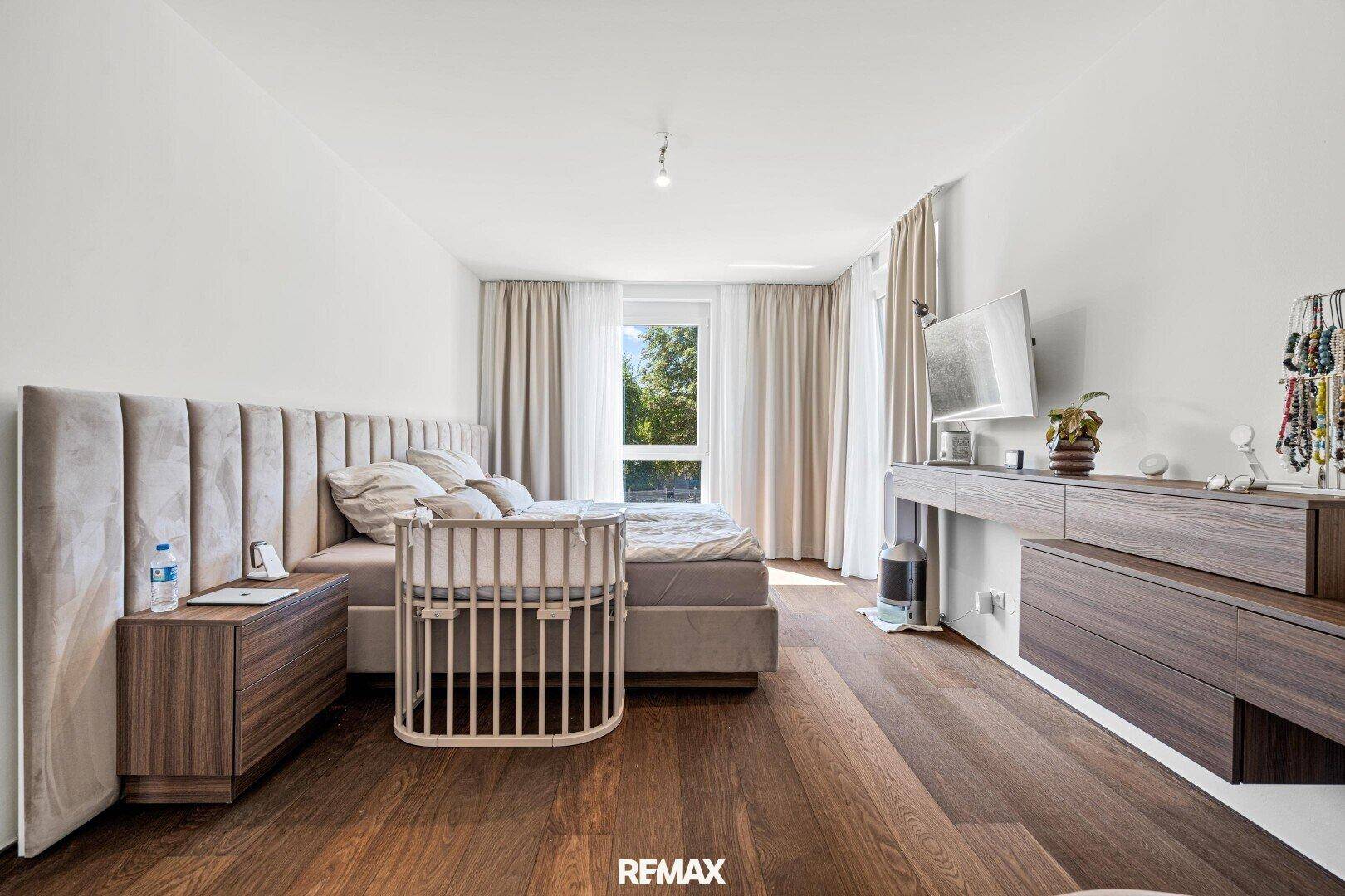 Geräumiges Schlafzimmer mit Holzboden, großem Bett und Fenster mit Blick ins Grüne.