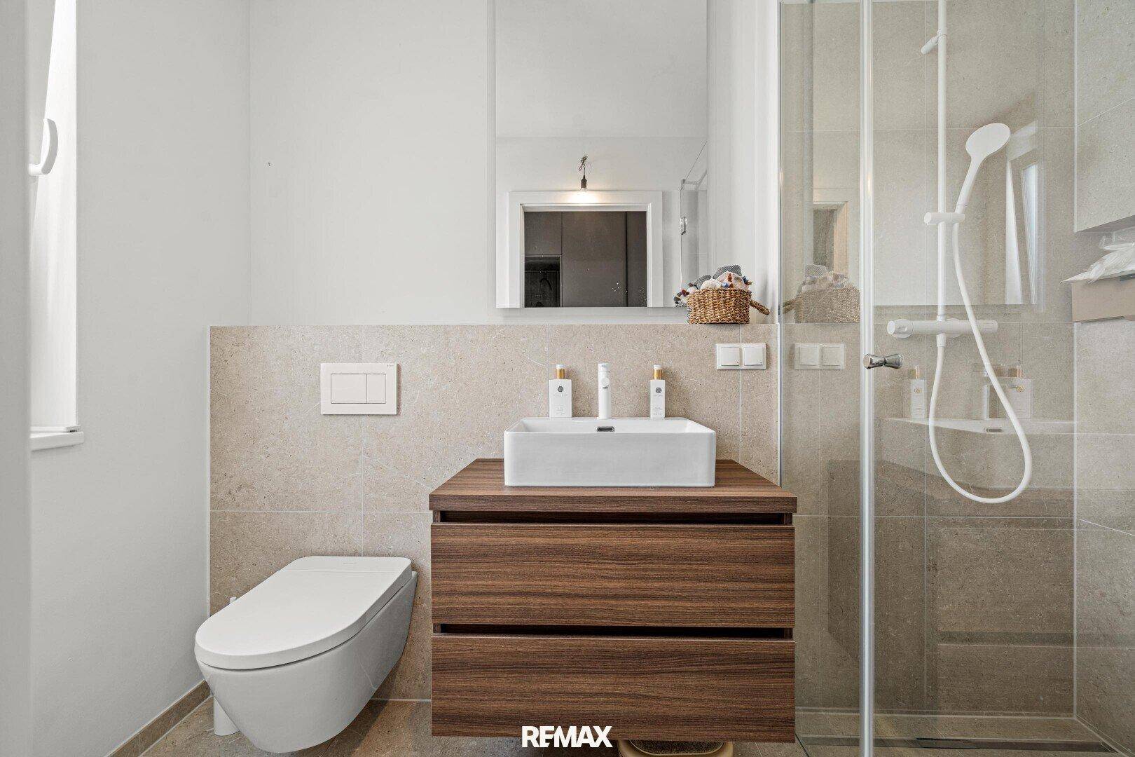 Helles Badezimmer mit Dusche, Waschtisch und WC, modern gefliest.