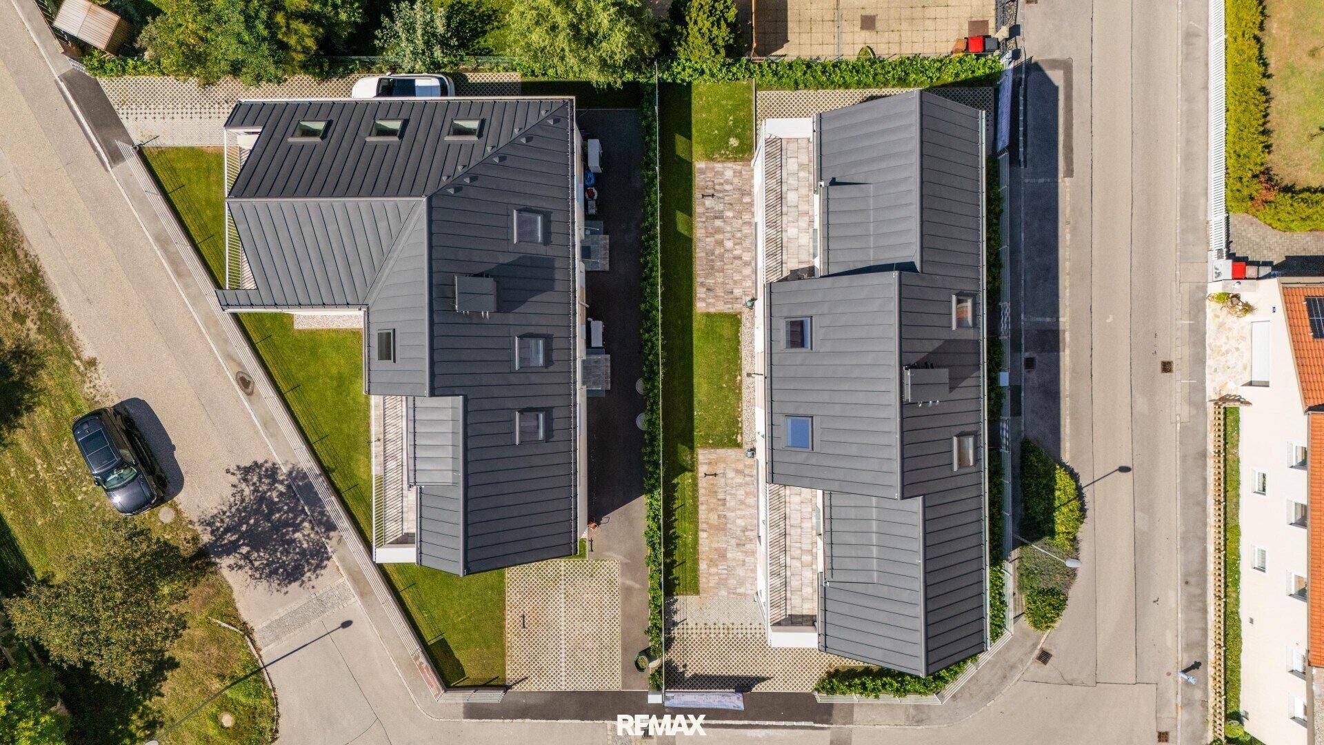 Vogelperspektive auf zwei moderne Gebäude mit Gärten und Parkplätzen.