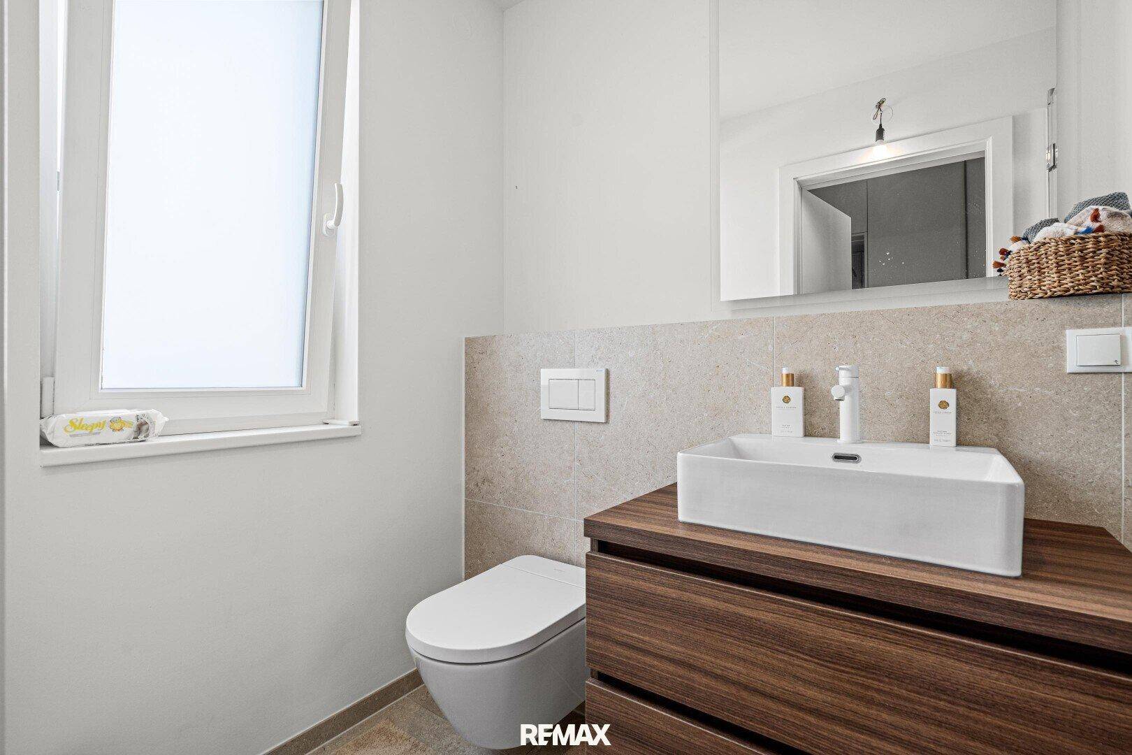 Modernes Badezimmer mit Waschtisch, WC und Fenster für Tageslicht.