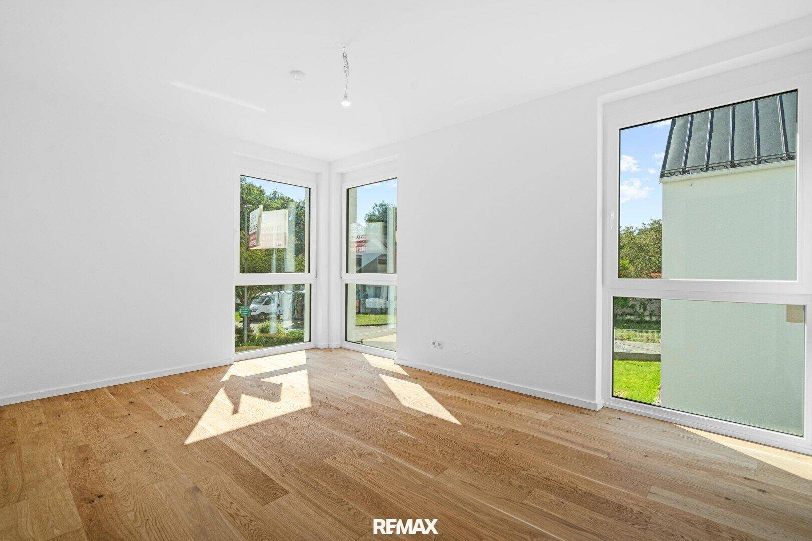 Helles Schlafzimmer mit Eichenparkett und mehreren Fenstern, die einen Blick ins Grüne bieten.