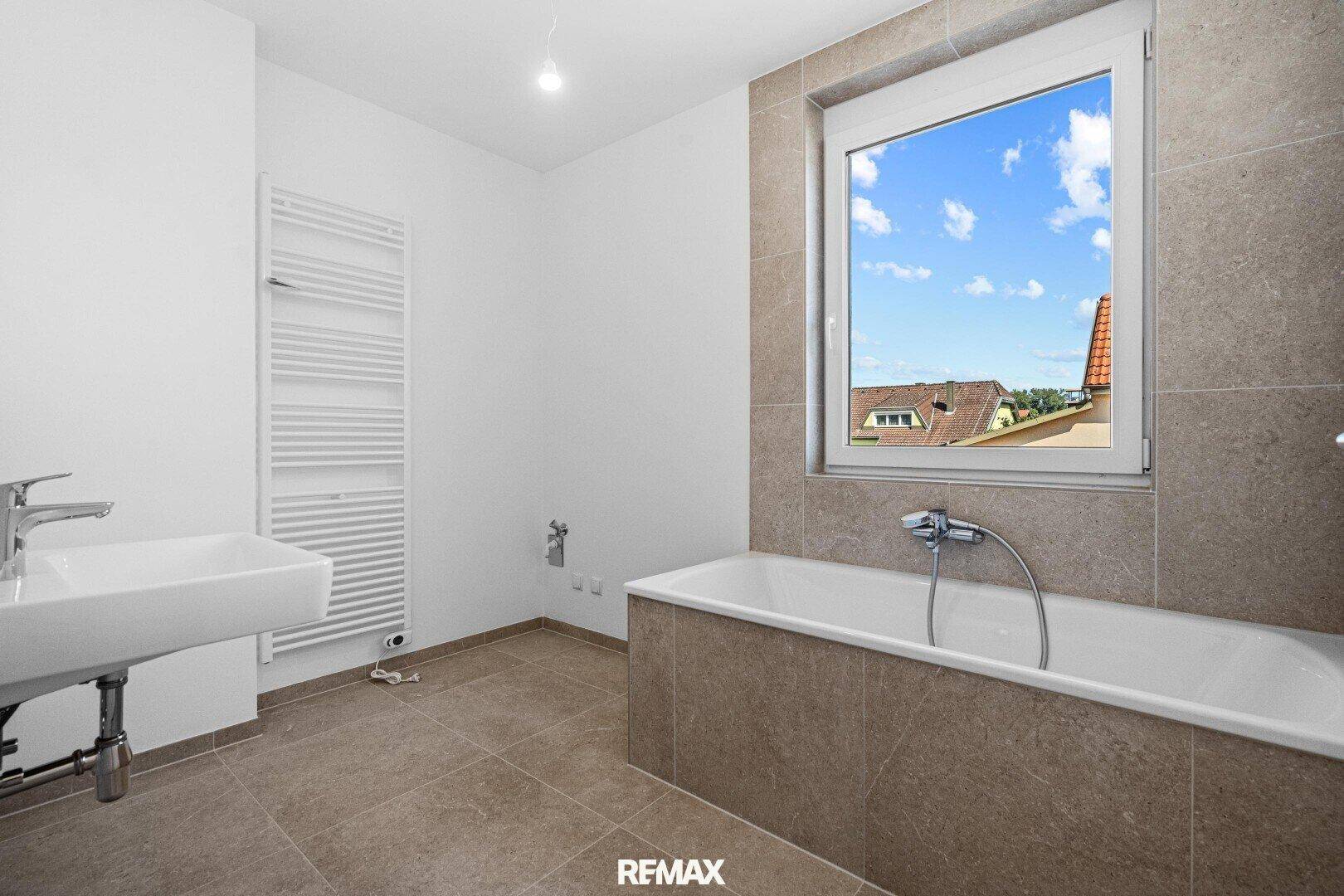 Modernes Badezimmer mit Badewanne, Waschbecken, beheiztem Handtuchhalter und Fenster.