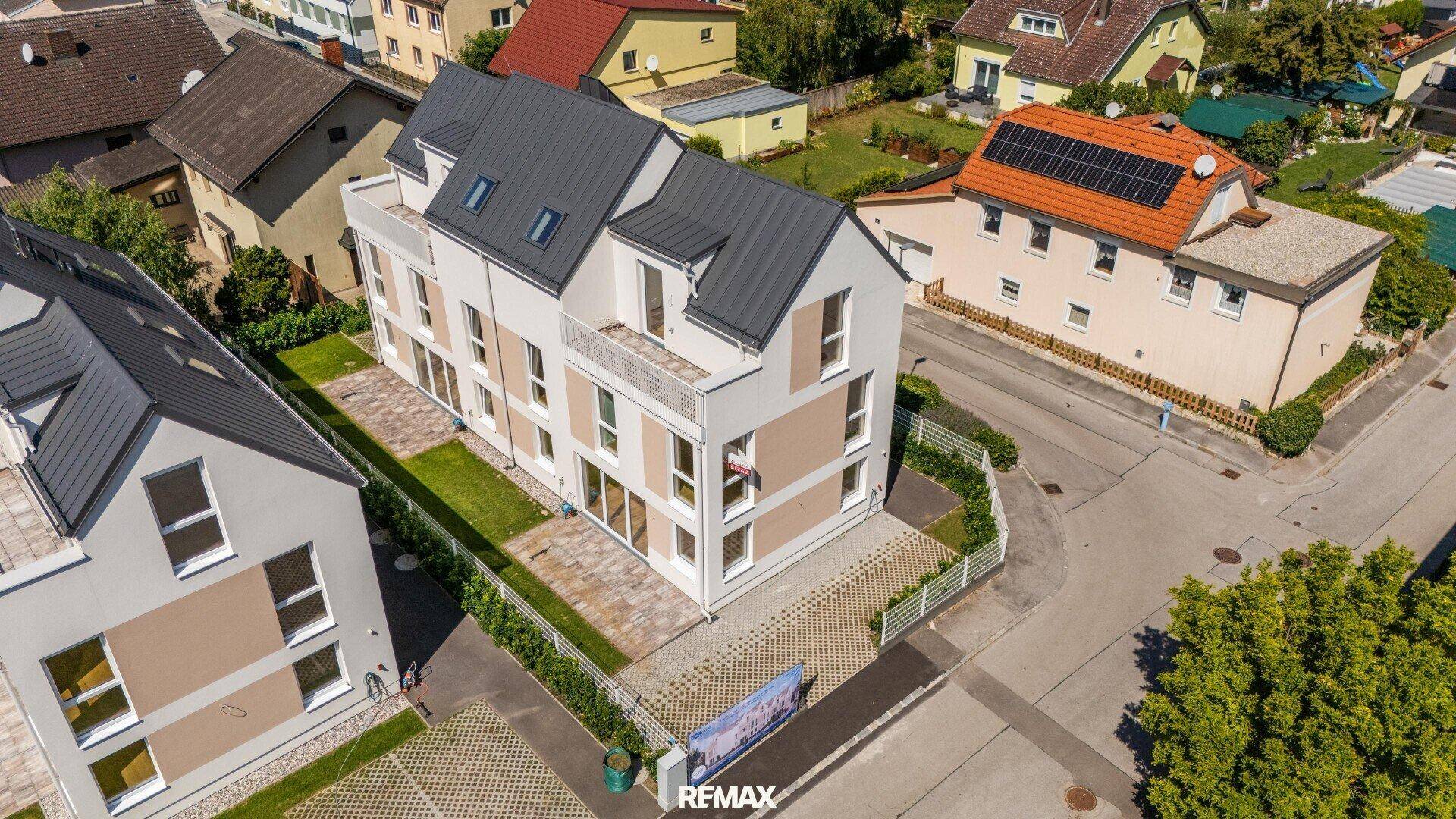 Vogelperspektive auf ein modernes Mehrfamilienhaus mit Balkonen und umliegenden Gärten.