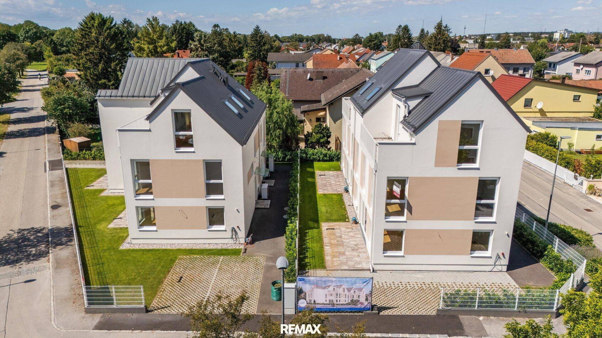 Zwei moderne Einfamilienhäuser mit Satteldach, Garten und Parkplätzen in ländlicher Umgebung.