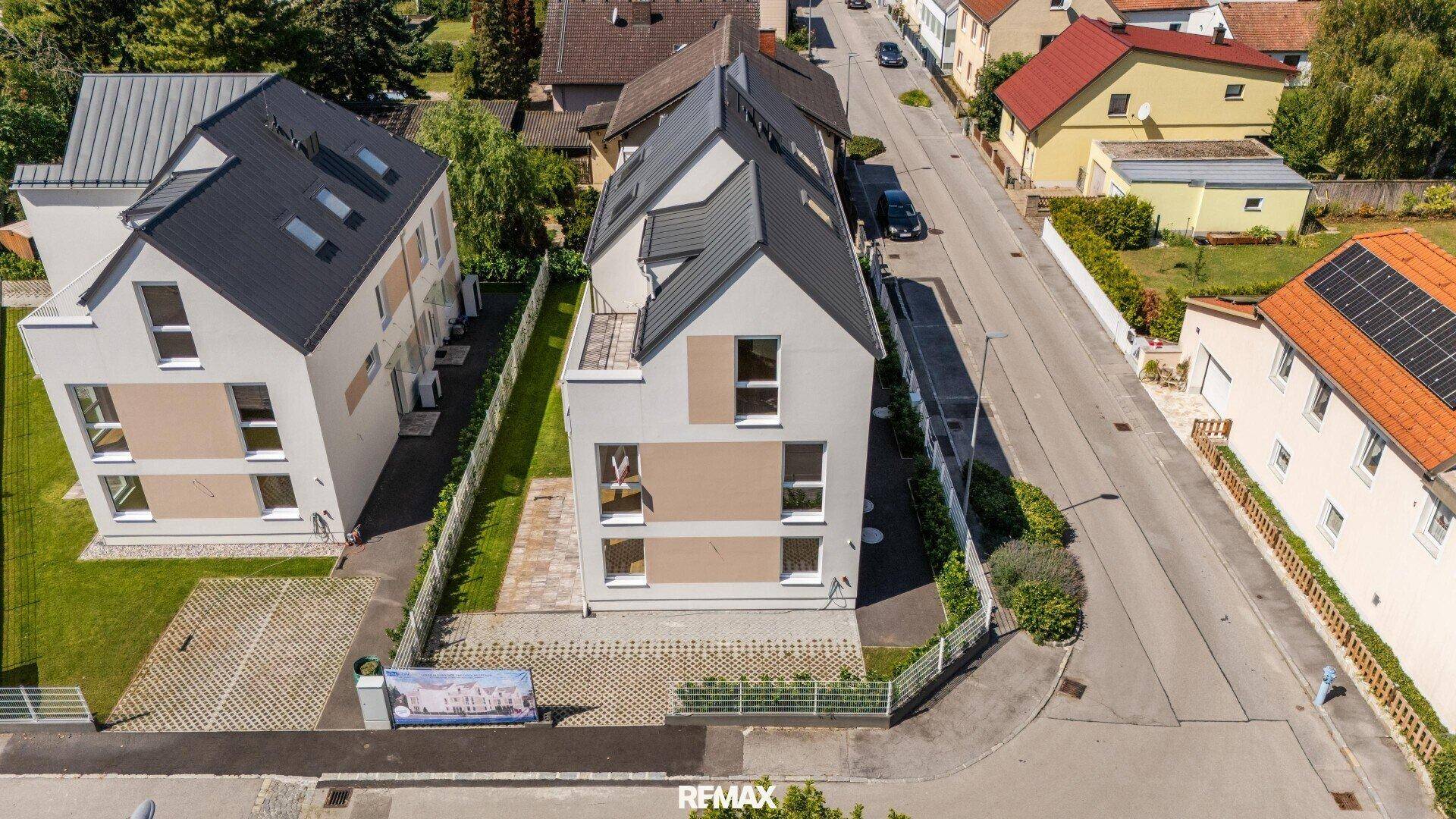 Luftaufnahme eines modernen Mehrfamilienhauses mit Satteldach und angrenzenden Parkplätzen.