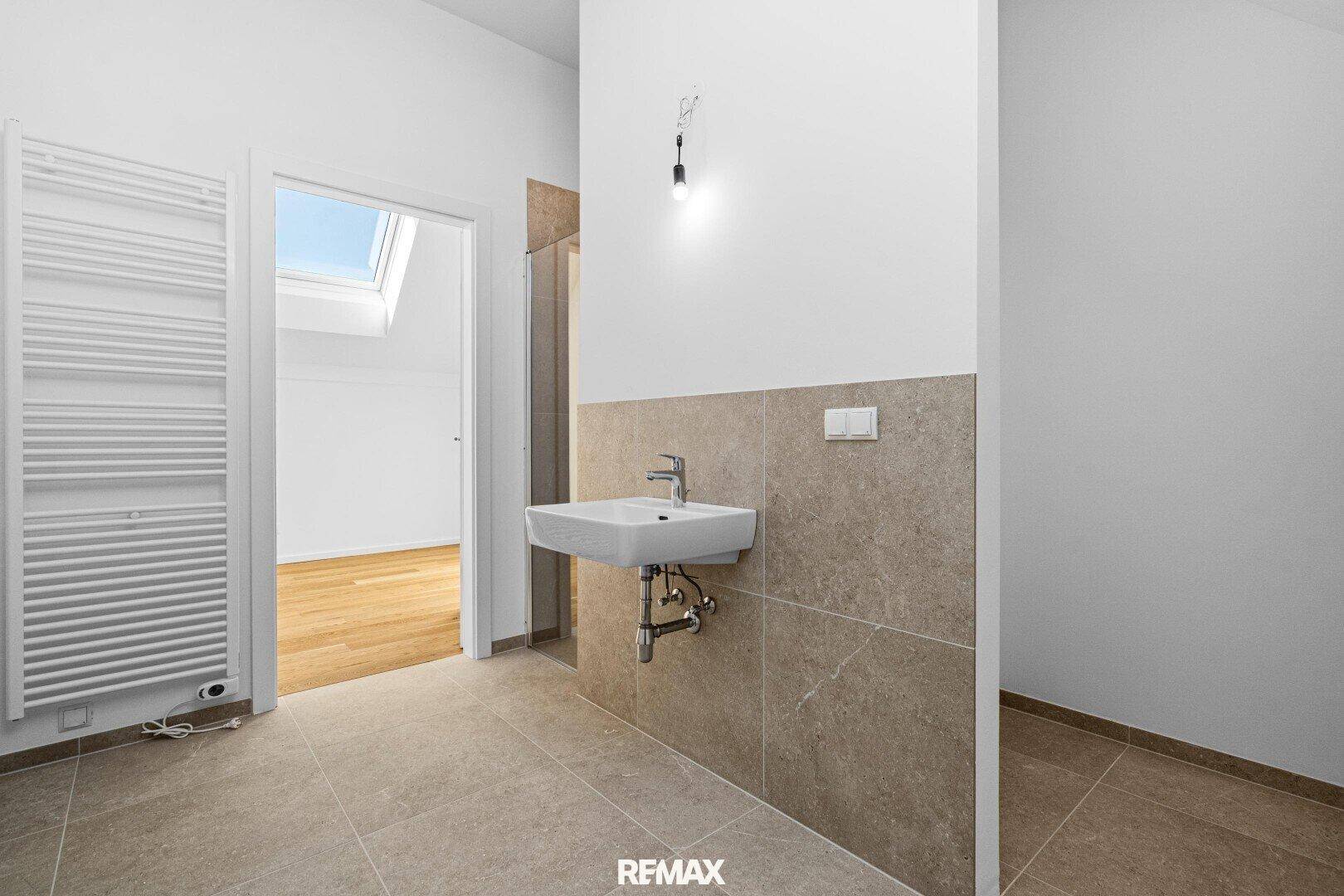 Modernes Badezimmer mit Waschbecken, beheiztem Handtuchhalter und Zugang zu einem weiteren Raum.