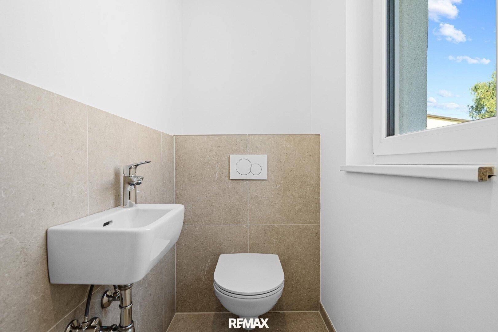 Gäste-WC mit Wand-WC, kleinem Waschbecken und Fenster für natürliche Belüftung.