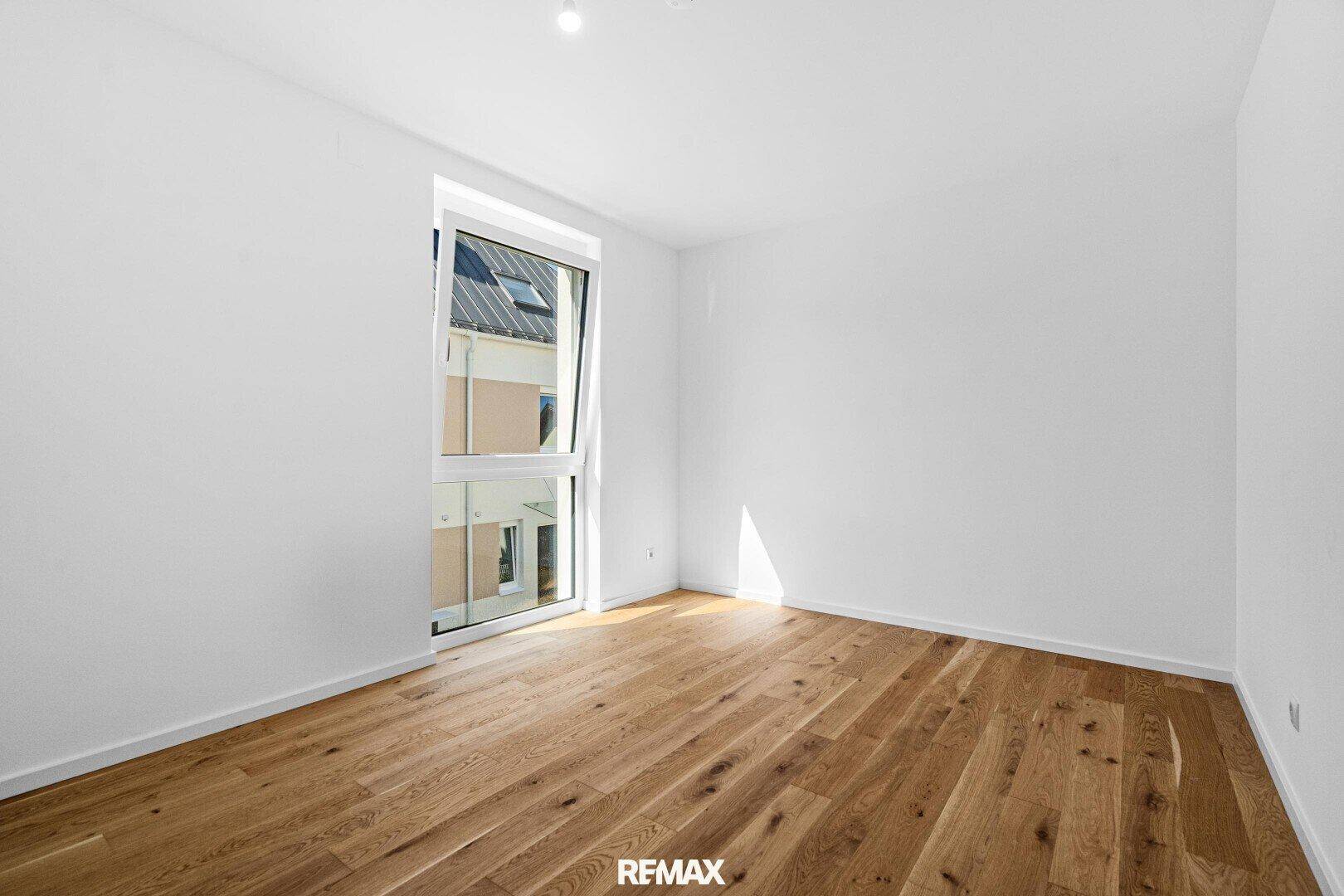 Schlafzimmer mit Eichenparkett und großem Fenster, das viel Licht in den Raum bringt.