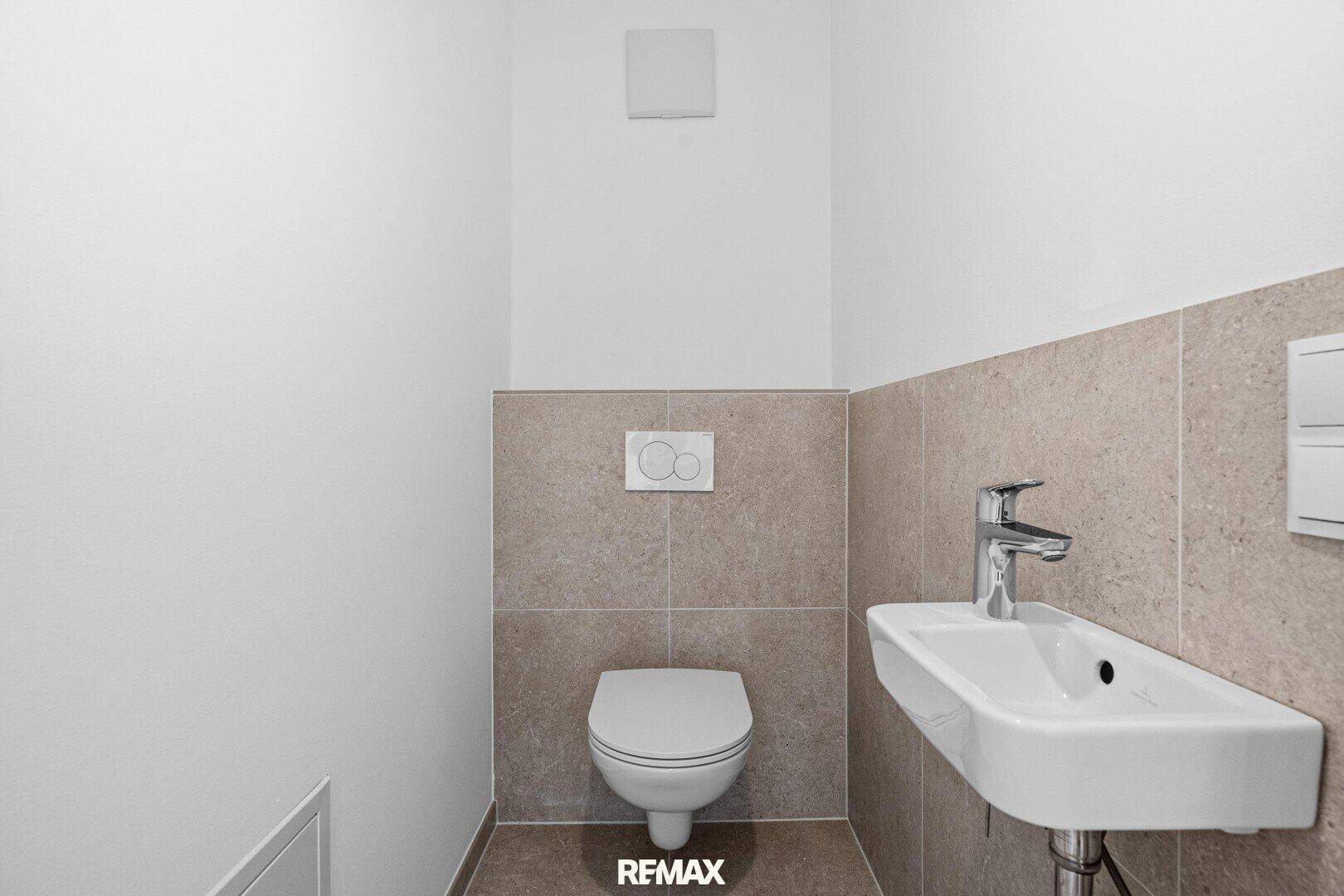 Modernes Gäste-WC mit Wand-WC, kleinem Waschbecken und hellen Fliesen an den Wänden.