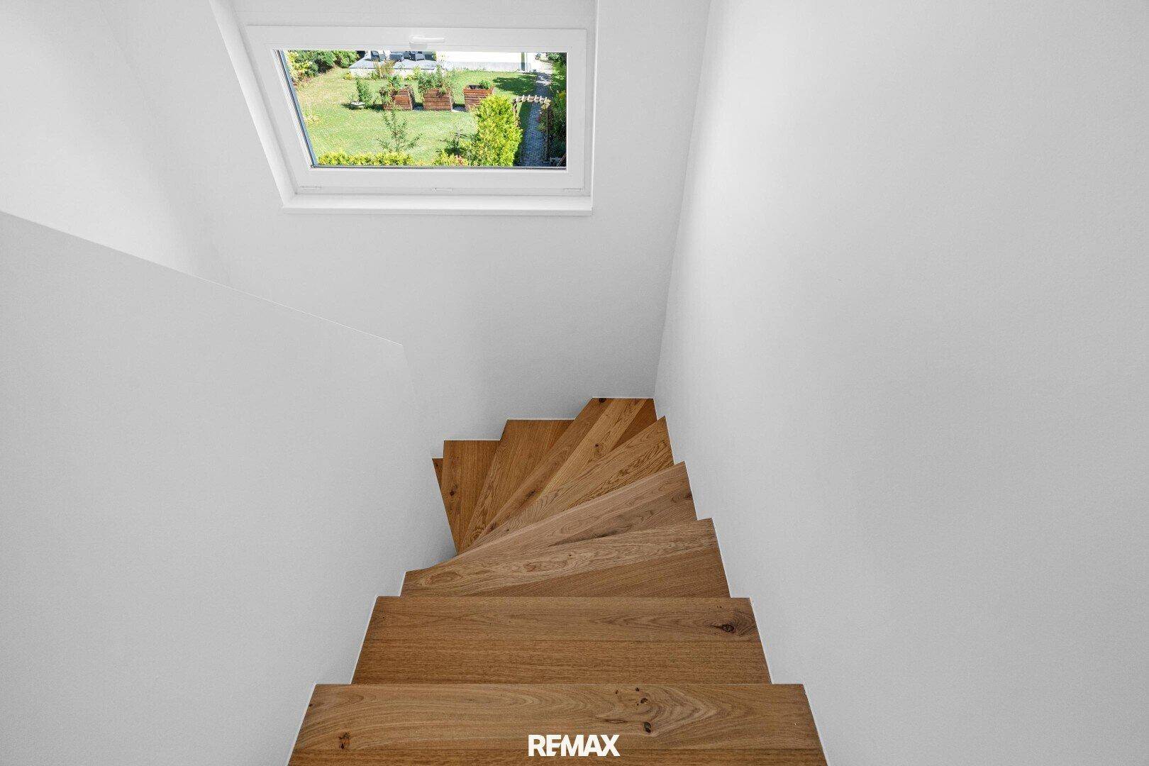 Holztreppe führt nach oben, mit einem Dachfenster, das einen Blick ins Grüne bietet.