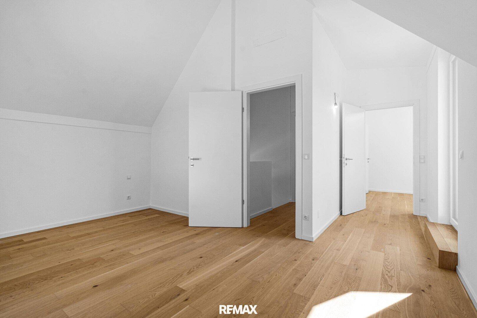 Geräumiges Dachzimmer mit Parkettboden, schrägen Wänden und mehreren Türen zu angrenzenden Räumen.