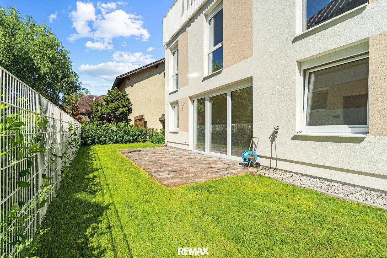 Kleiner Gartenbereich mit Rasenfläche und gepflasterter Terrasse vor großen Glasschiebetüren.