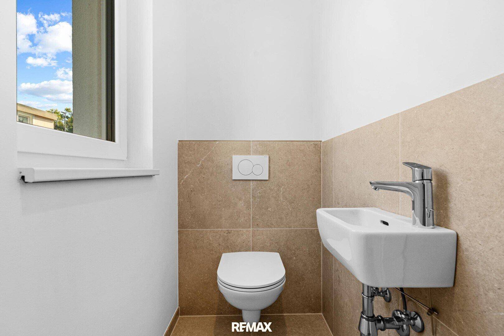 Modernes Gäste-WC mit wandhängendem WC, kleinem Waschbecken und beigefarbenen Fliesen.