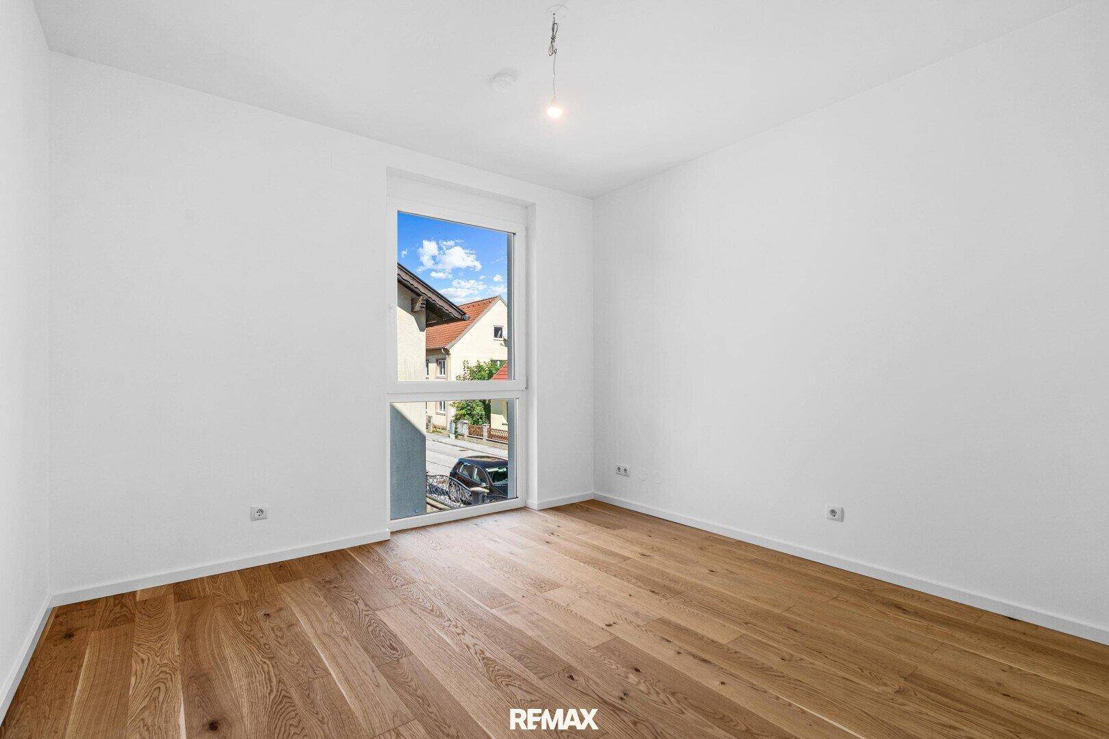 Geräumiges Schlafzimmer mit Holzboden und einem hohen Fenster, das viel Licht hereinlässt.