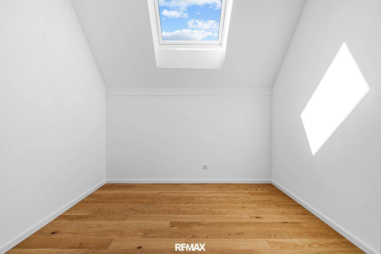 Helles Dachzimmer mit schrägen Wänden, Parkettboden und einem Dachfenster für viel Licht.