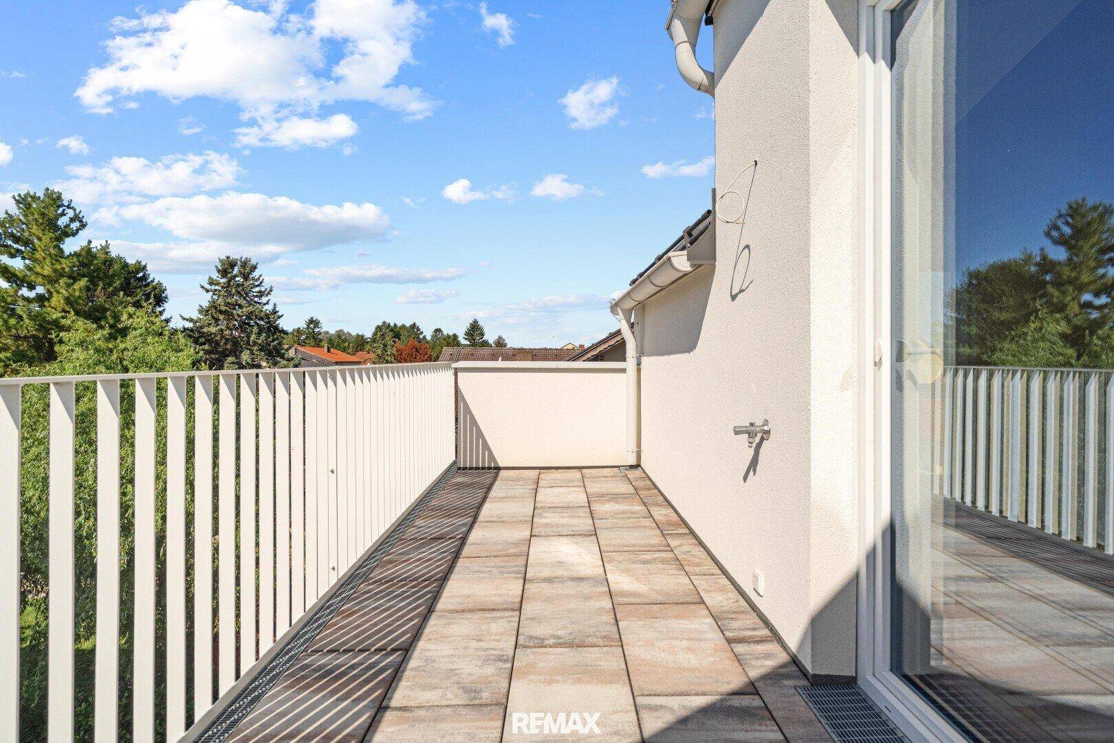 Geräumiger Balkon mit Fliesenboden und weißem Geländer, bietet einen weiten Blick ins Grüne.